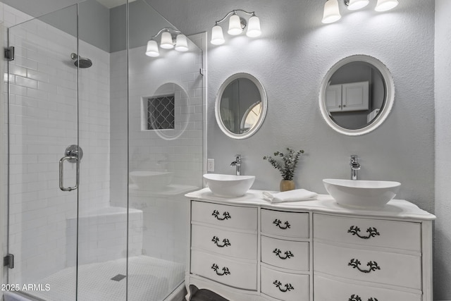 full bath featuring a sink, a textured wall, a stall shower, and double vanity