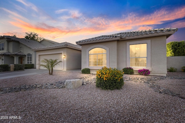 mediterranean / spanish-style house with a garage, stucco siding, driveway, and a tile roof