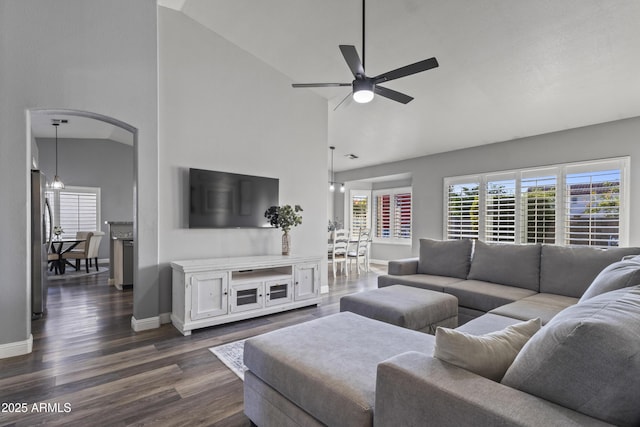 living room featuring baseboards, ceiling fan, high vaulted ceiling, dark wood-type flooring, and arched walkways