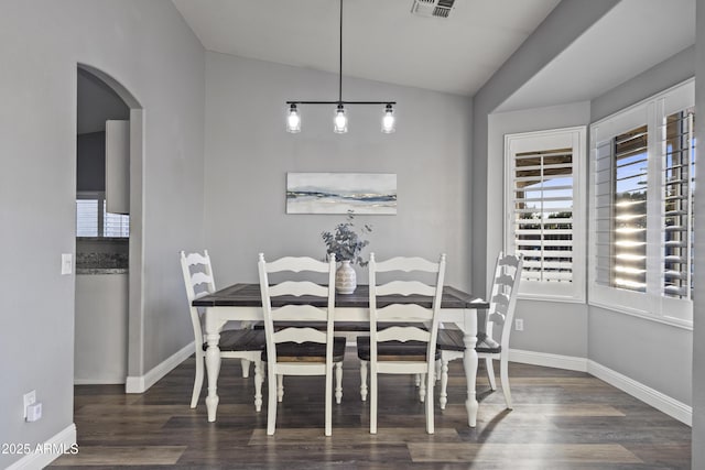 dining room featuring visible vents, arched walkways, lofted ceiling, and wood finished floors
