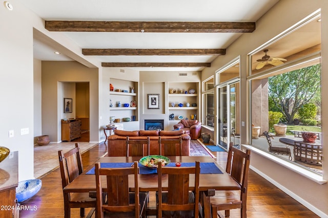 dining room featuring baseboards, built in features, a ceiling fan, a glass covered fireplace, and wood finished floors