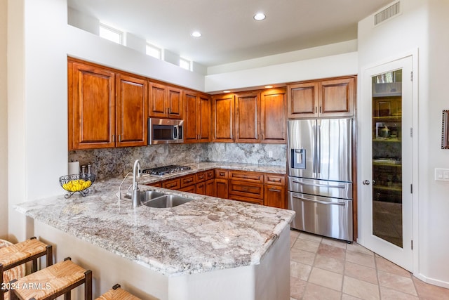 kitchen with stainless steel appliances, a peninsula, a sink, decorative backsplash, and brown cabinetry