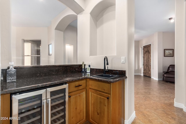 kitchen with dark stone counters, beverage cooler, light tile patterned flooring, and sink