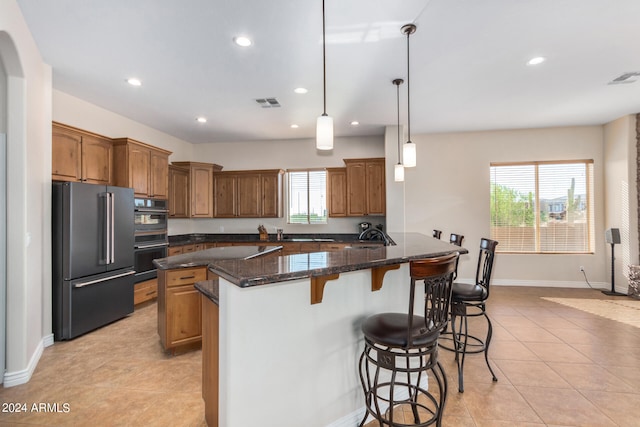 kitchen featuring stainless steel refrigerator, light tile patterned floors, a center island, black double oven, and decorative light fixtures