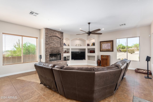 tiled living room with a healthy amount of sunlight, a fireplace, ceiling fan, and built in shelves