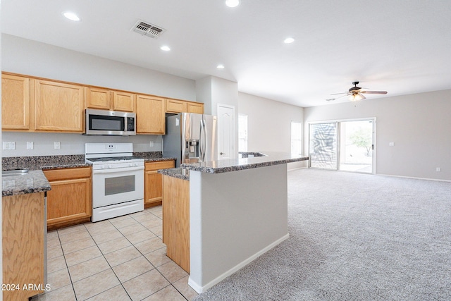 kitchen featuring a kitchen island, light carpet, appliances with stainless steel finishes, dark stone countertops, and ceiling fan