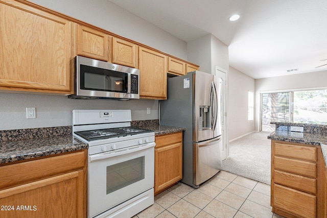 kitchen featuring dark stone counters, stainless steel appliances, light colored carpet, and light brown cabinetry