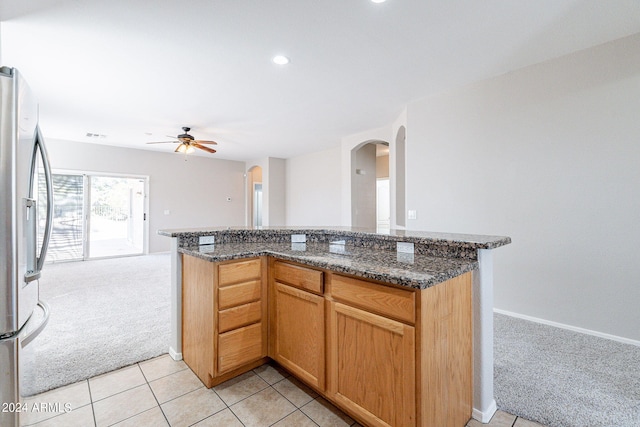 kitchen with dark stone counters, kitchen peninsula, light carpet, ceiling fan, and stainless steel fridge