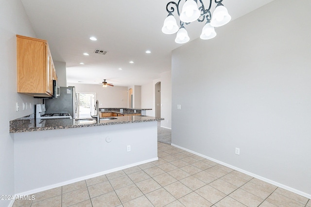 kitchen with hanging light fixtures, ceiling fan with notable chandelier, kitchen peninsula, white stove, and dark stone counters