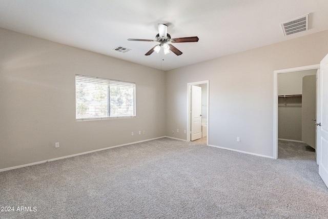 unfurnished bedroom with ceiling fan, a closet, a spacious closet, light carpet, and ensuite bath