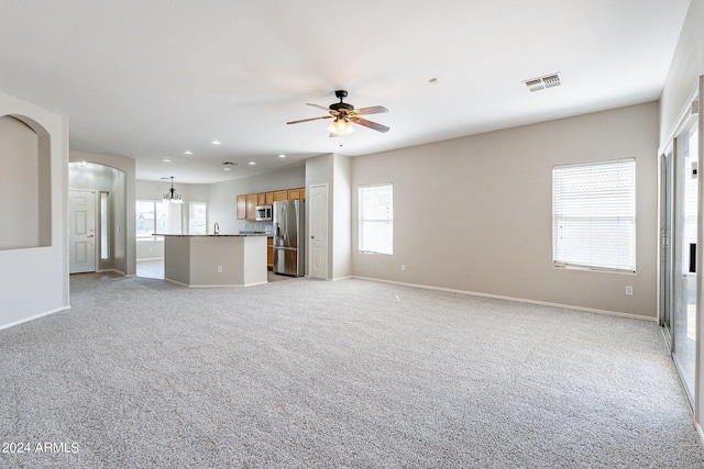 unfurnished living room with ceiling fan with notable chandelier, light colored carpet, and plenty of natural light