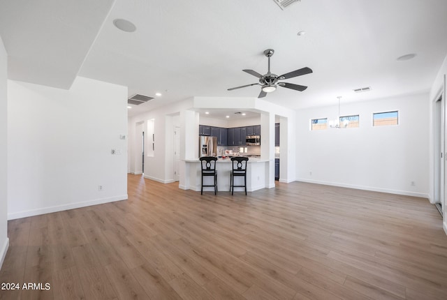 unfurnished living room with ceiling fan with notable chandelier and light hardwood / wood-style floors