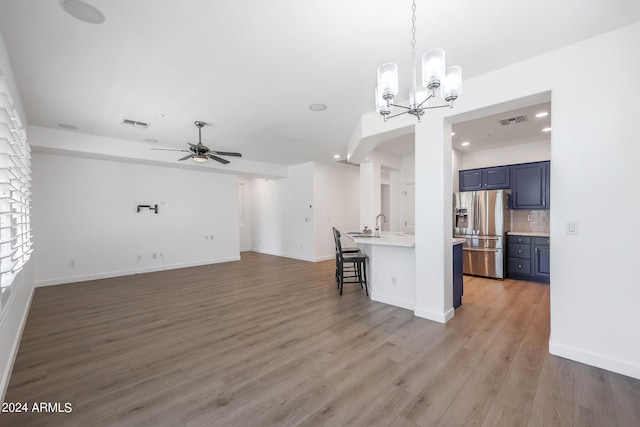 kitchen with light wood-type flooring, a kitchen breakfast bar, stainless steel refrigerator with ice dispenser, tasteful backsplash, and ceiling fan with notable chandelier