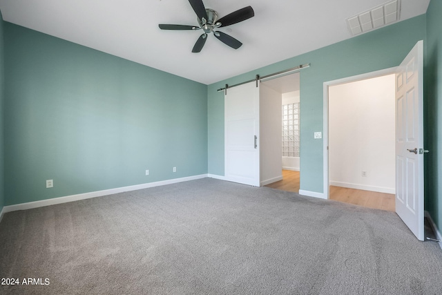 unfurnished bedroom featuring ceiling fan, light carpet, and a barn door