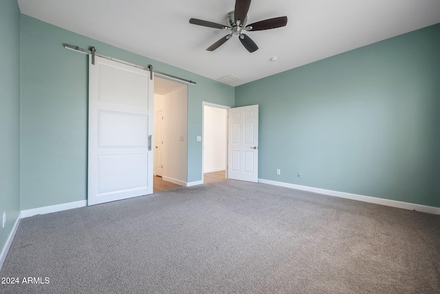 unfurnished bedroom featuring carpet floors, ceiling fan, and a barn door