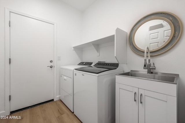 laundry area featuring sink, light hardwood / wood-style floors, independent washer and dryer, and cabinets