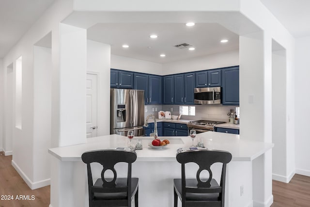 kitchen featuring a kitchen bar, light wood-type flooring, decorative backsplash, an island with sink, and stainless steel appliances