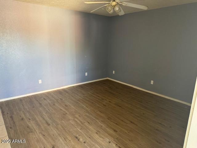 spare room with dark wood-style floors, ceiling fan, and baseboards