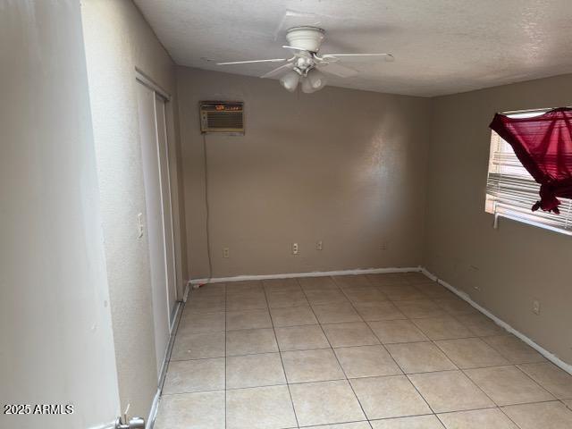 unfurnished room with a textured ceiling, light tile patterned floors, a ceiling fan, baseboards, and a wall mounted air conditioner