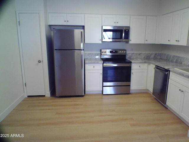 kitchen featuring stainless steel appliances, white cabinets, light wood-type flooring, and light stone countertops