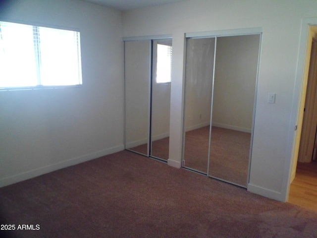 unfurnished bedroom featuring baseboards, multiple closets, and carpet