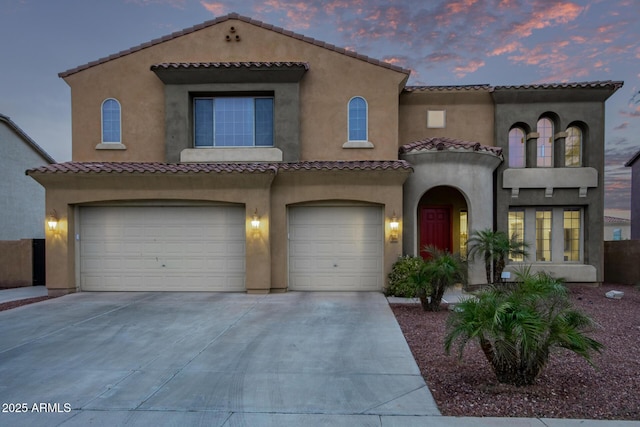 mediterranean / spanish house with stucco siding, driveway, an attached garage, and a tiled roof