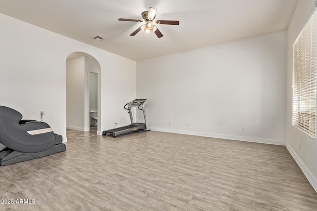 workout area with visible vents, a ceiling fan, arched walkways, light wood-style floors, and baseboards