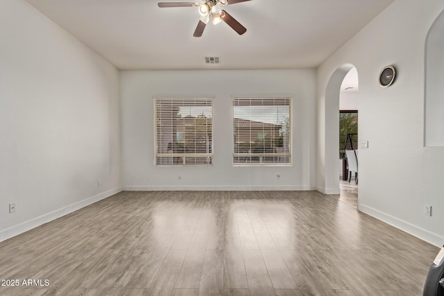 unfurnished room with a ceiling fan, wood finished floors, visible vents, baseboards, and arched walkways