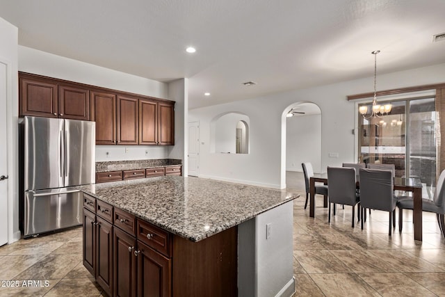 kitchen with a kitchen island, a chandelier, stone counters, freestanding refrigerator, and arched walkways