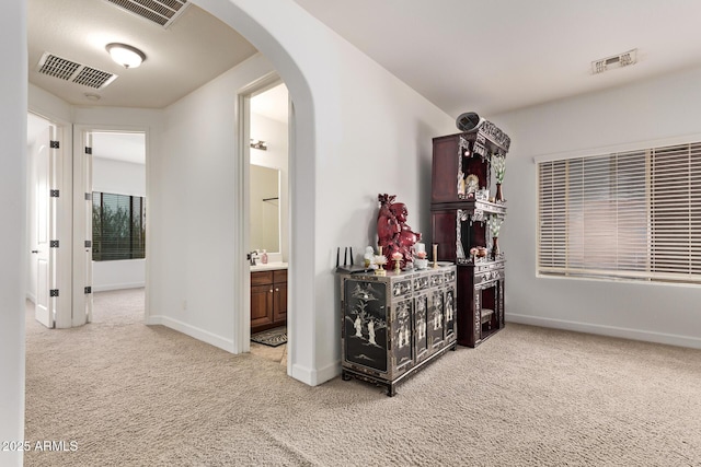 corridor featuring visible vents, arched walkways, light colored carpet, and baseboards