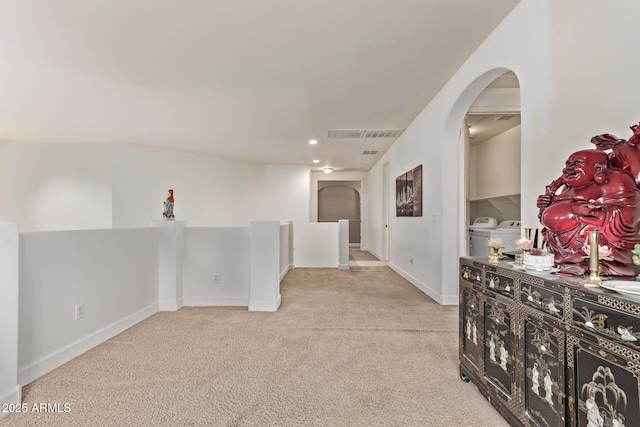 corridor featuring visible vents, arched walkways, light colored carpet, and washing machine and dryer