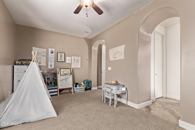 recreation room featuring carpet flooring, a ceiling fan, arched walkways, and baseboards