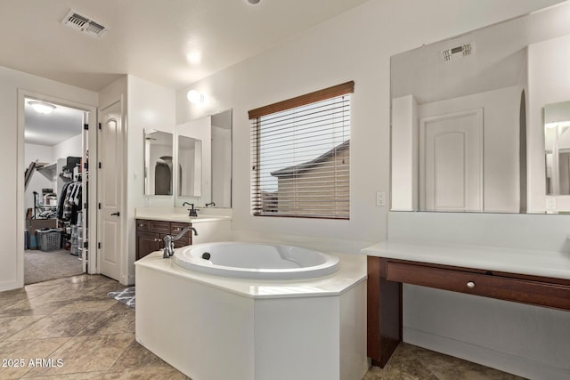 full bath featuring visible vents, vanity, a walk in closet, and a garden tub