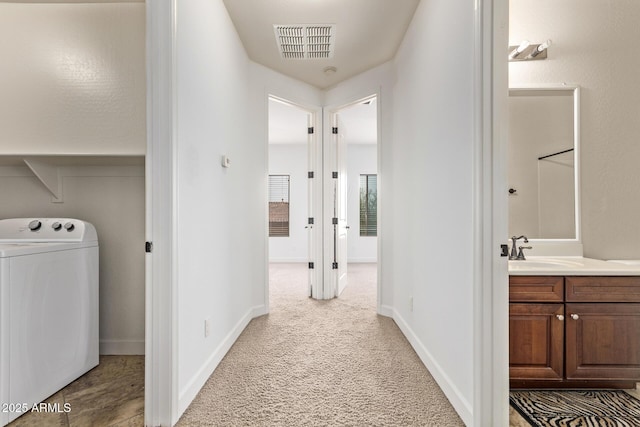 hallway with visible vents, baseboards, carpet flooring, washer / dryer, and a sink