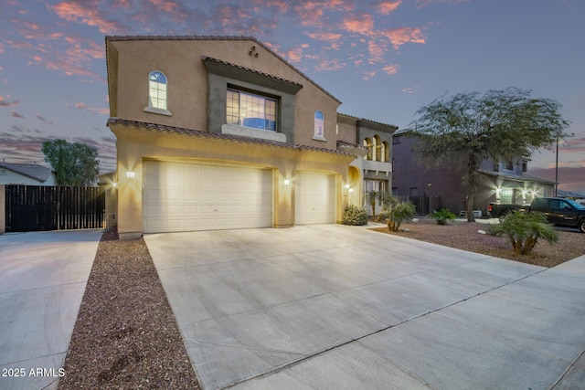 mediterranean / spanish house featuring fence, a tile roof, concrete driveway, stucco siding, and an attached garage