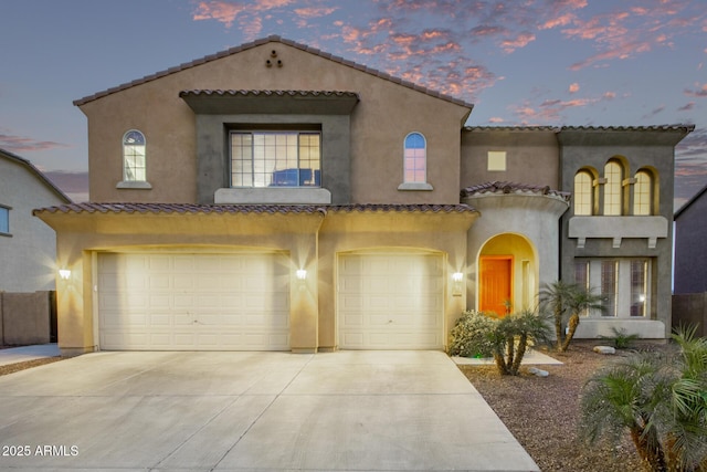 mediterranean / spanish house featuring a tiled roof, a garage, driveway, and stucco siding