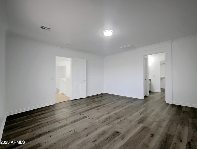 unfurnished bedroom featuring dark hardwood / wood-style floors, ornamental molding, connected bathroom, and a spacious closet