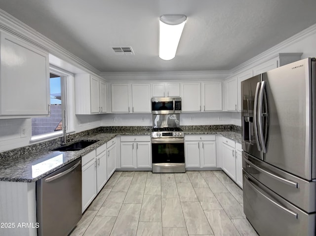 kitchen with sink, crown molding, appliances with stainless steel finishes, white cabinetry, and dark stone counters