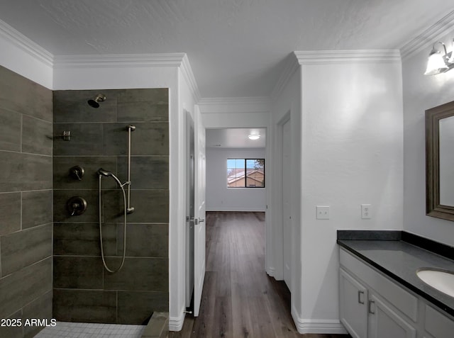 bathroom with hardwood / wood-style flooring, vanity, a tile shower, and crown molding