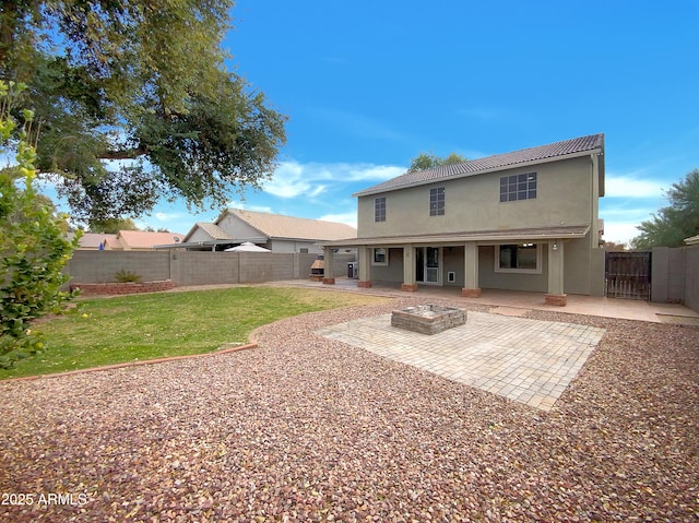 back of property with a yard, a patio area, and a fire pit