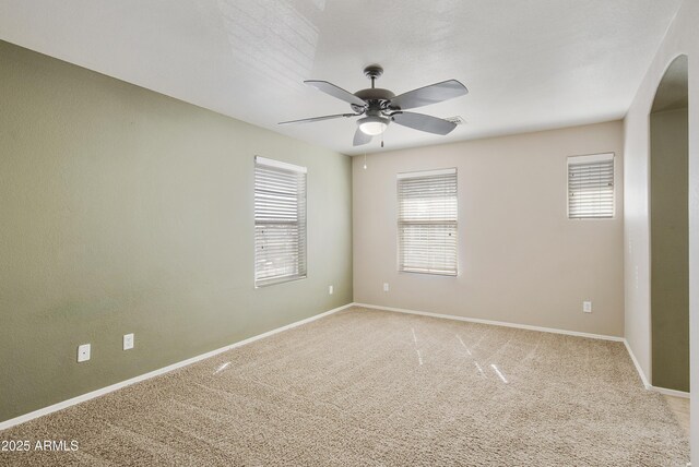 unfurnished room featuring arched walkways, a ceiling fan, baseboards, and light carpet
