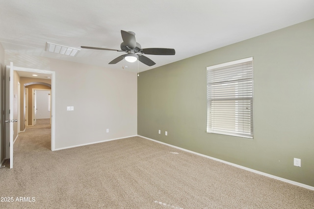 spare room featuring visible vents, a ceiling fan, light carpet, arched walkways, and baseboards
