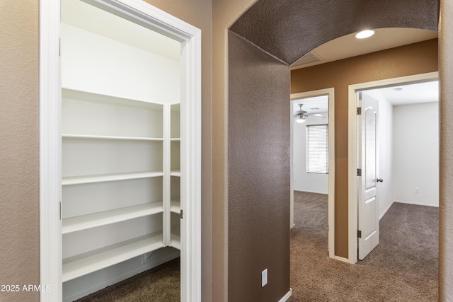 corridor featuring baseboards, a textured wall, and carpet flooring