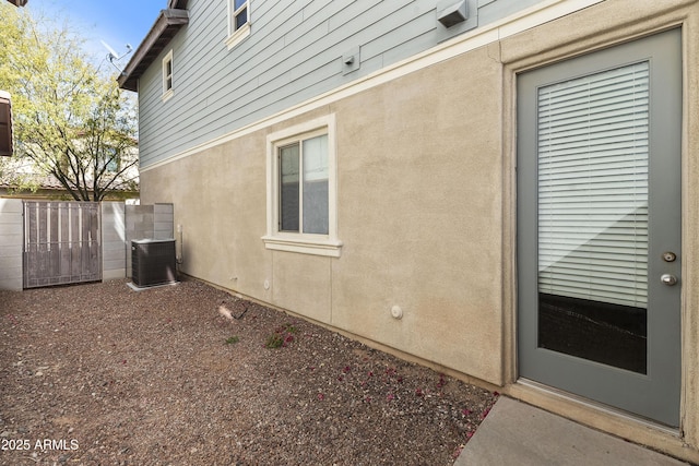 view of side of home featuring fence, cooling unit, and stucco siding