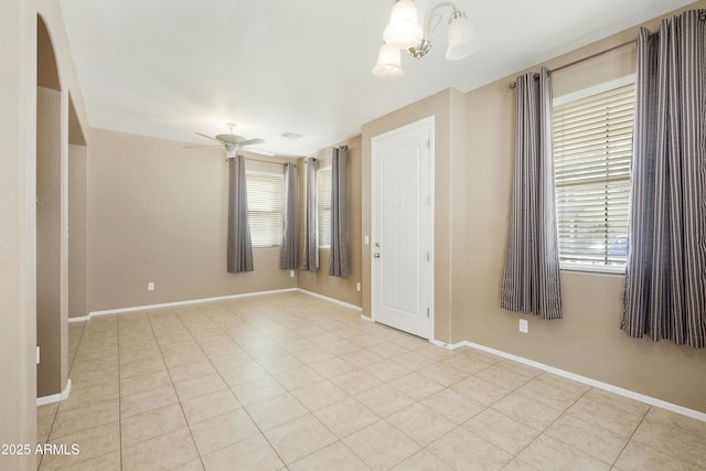 empty room with light tile patterned flooring, arched walkways, baseboards, and ceiling fan with notable chandelier