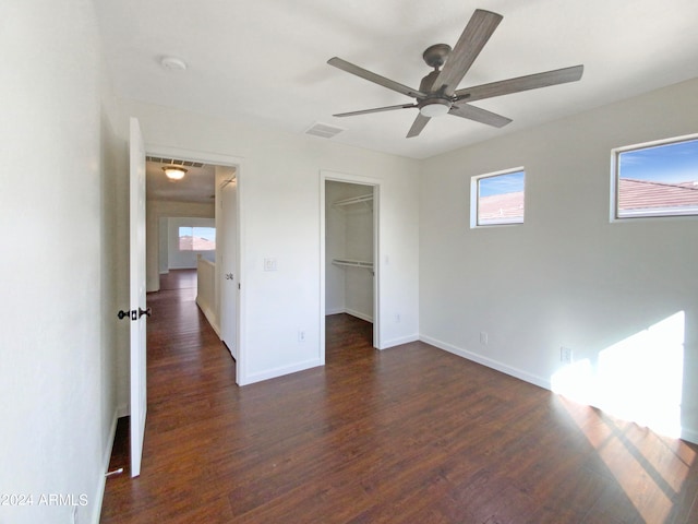 unfurnished bedroom with dark hardwood / wood-style flooring, a closet, a spacious closet, and ceiling fan