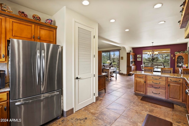 kitchen featuring hanging light fixtures, tile patterned flooring, an inviting chandelier, light stone countertops, and stainless steel fridge