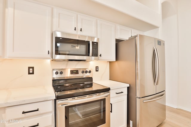 kitchen with appliances with stainless steel finishes, white cabinetry, decorative backsplash, light wood-type flooring, and light stone counters