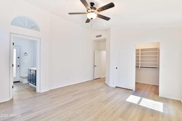 unfurnished bedroom featuring vaulted ceiling, light hardwood / wood-style floors, ensuite bath, a walk in closet, and a closet