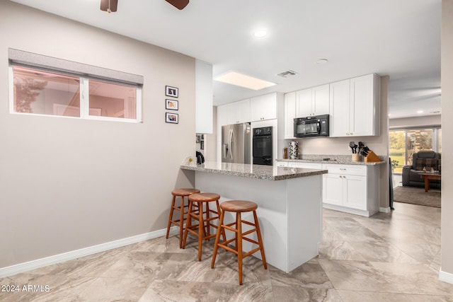 kitchen featuring black appliances, a kitchen breakfast bar, kitchen peninsula, light stone counters, and white cabinetry